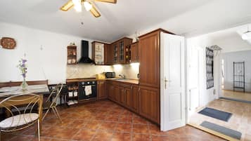 Une cuisine avec un sol carrelé, des meubles de rangement en bois, une cuisinière noire et un ventilateur de plafond.