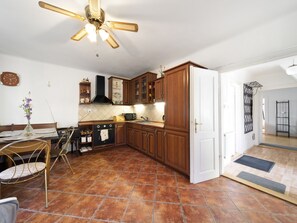 Une cuisine avec un sol carrelé, des meubles de rangement en bois, une cuisinière noire et un ventilateur de plafond.