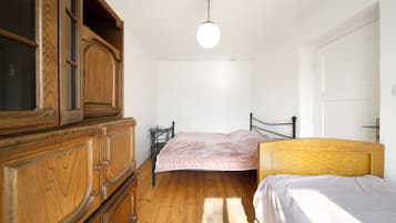 Une chambre avec une commode en bois, un lit recouvert d’une couverture rose et une tête de lit en bois.