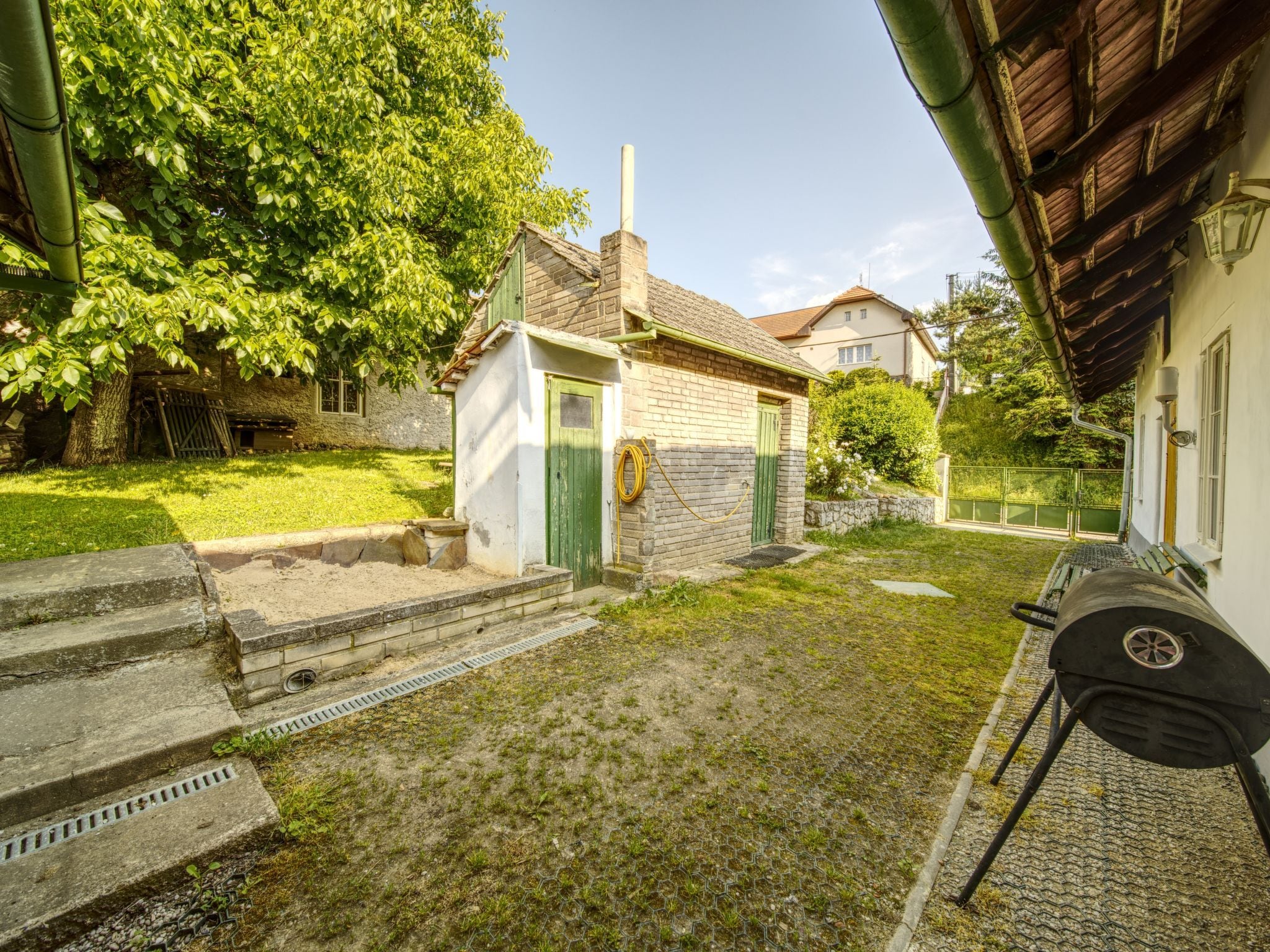 Une petite maison avec une porte verte, une cheminée en briques et une cour verdoyante avec des marches menant à la porte.