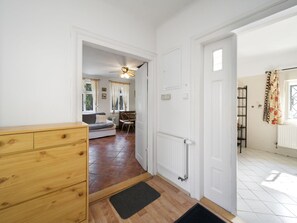 Un pasillo que conduce a una sala de estar con un sofá, una silla y una mesa de comedor. Hay un aparador de madera y un radiador en la pared.