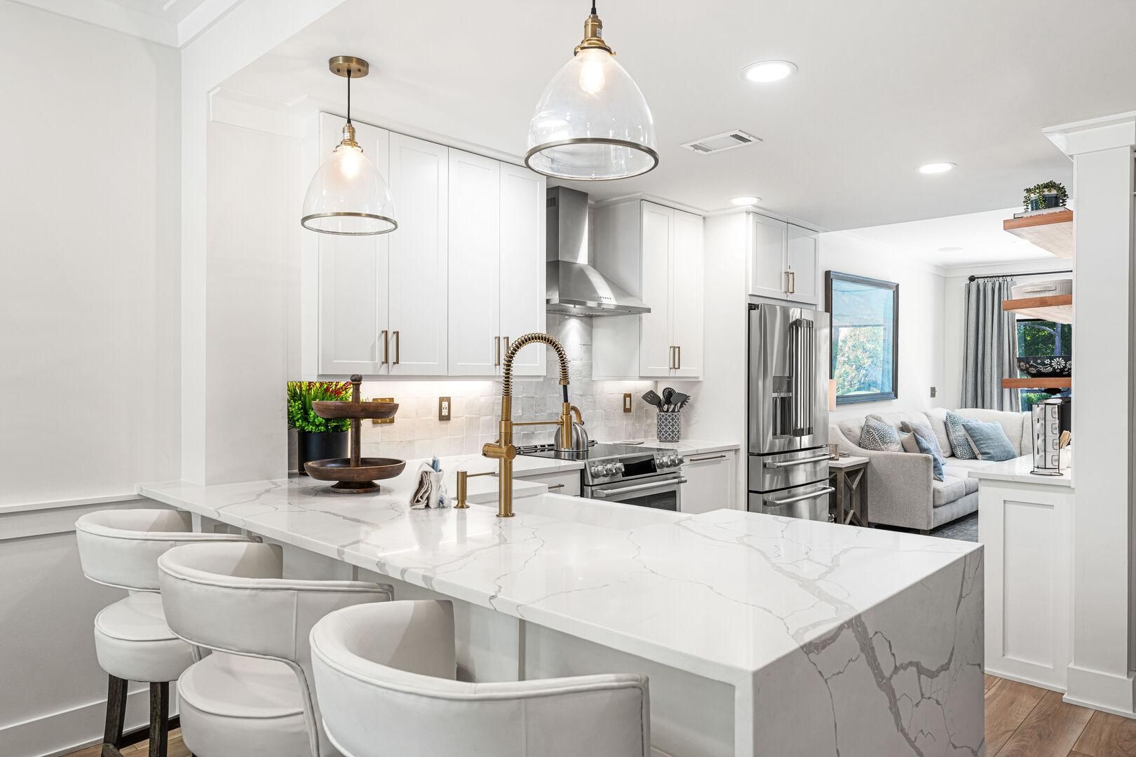 A modern kitchen with white cabinetry, a marble island, stainless steel appliances, and pendant lighting.