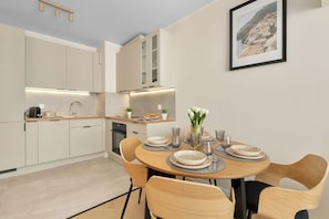 Una cocina moderna con electrodomésticos integrados, un comedor con una mesa redonda y sillas, y una fotografía enmarcada de la costa en la pared.
