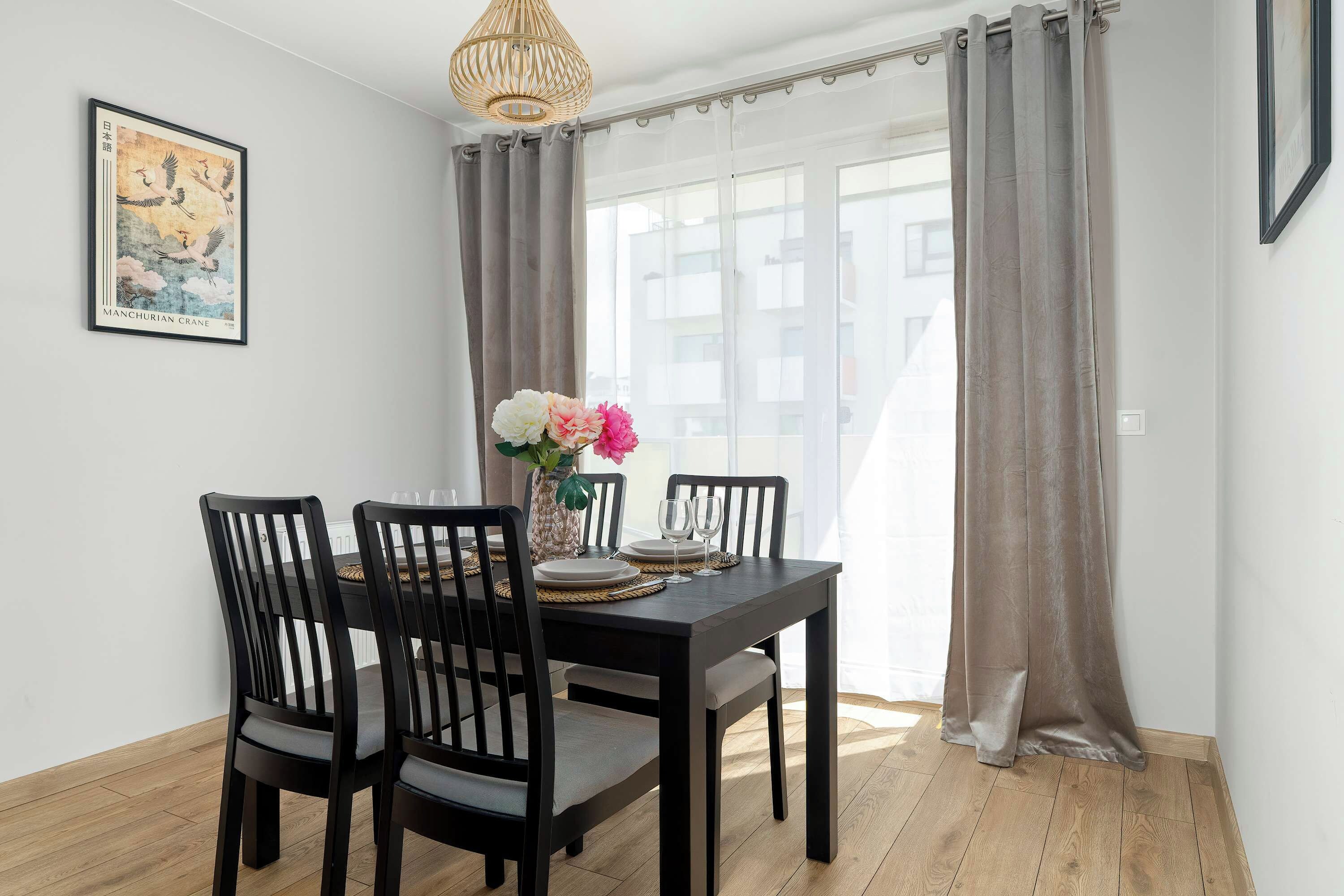 Een eetruimte met een tafel voor vier personen, een vaas met bloemen en een kunstwerk in een lijst aan de muur.