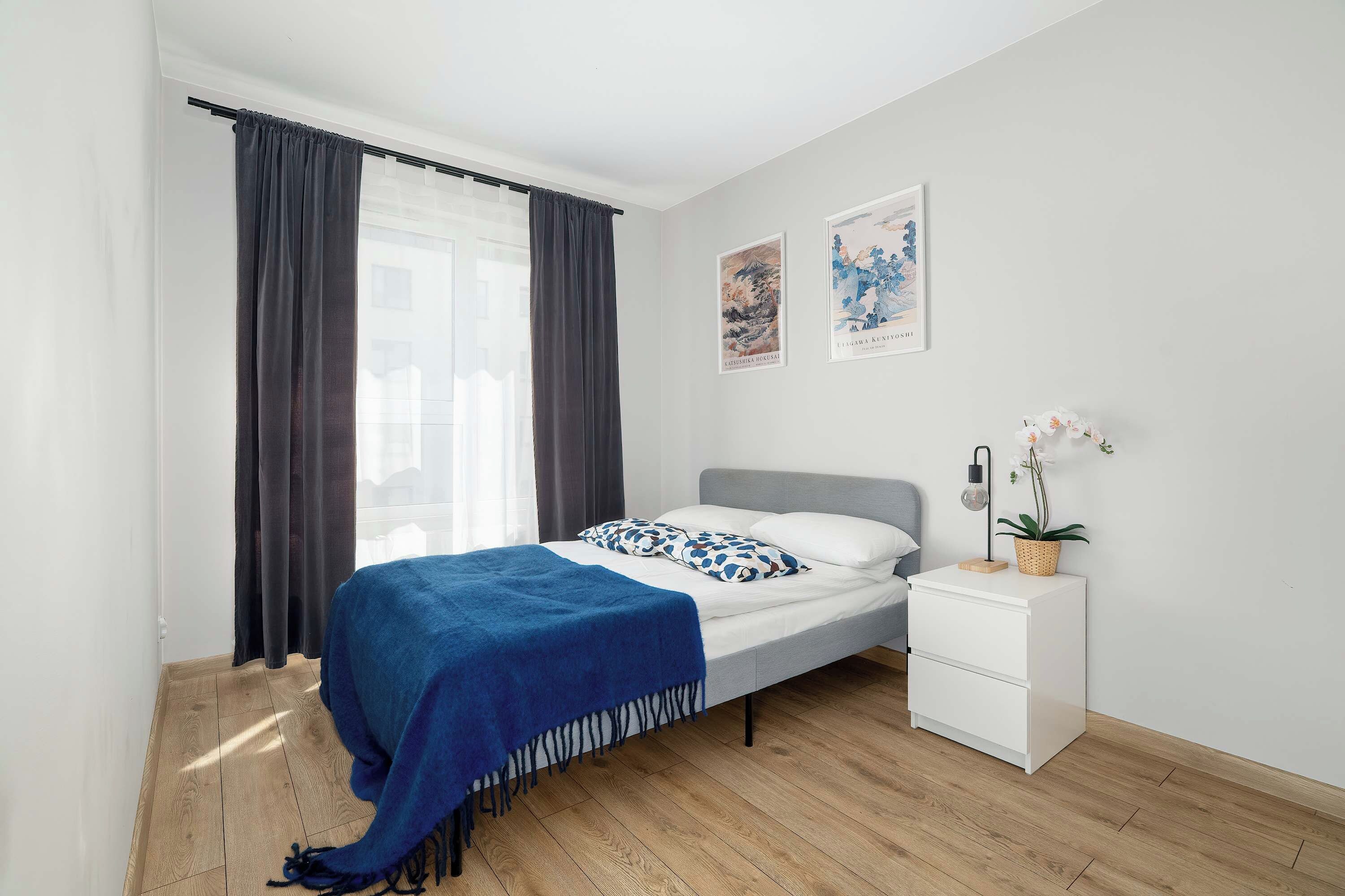 A bedroom with a bed, a nightstand, a potted plant, and two wall art pieces.
