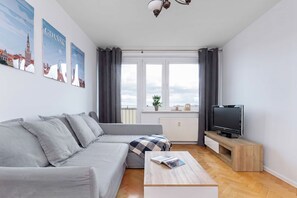 Ein modernes Wohnzimmer mit einem grauen Sofa, einem Couchtisch, einem Fernseher auf einem Holzschrank und einem Fenster mit Vorhängen.