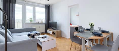 Una sala de estar moderna con sofá, mesa de centro, televisión y comedor con sillas y mesa para dos.