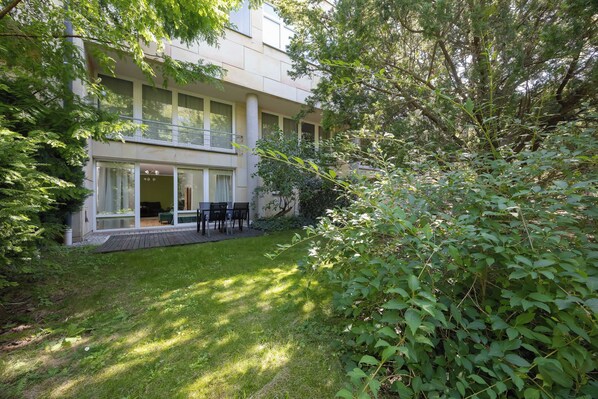 Ein modernes Gebäude mit einem Balkon, einer überdachten Außen-Sitzgelegenheit und einem gepflegten Rasen.
