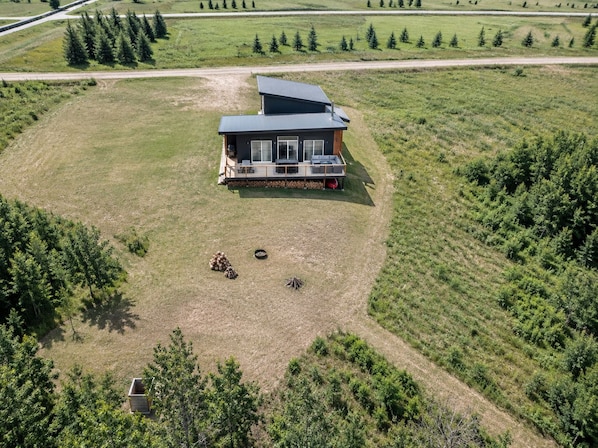 A modern cabin with a deck, surrounded by a grassy field and trees. - Big Shell Lake Cabin | Sleeps 8 | Fireplace, Starlink & Private Yard (Shell Lake)
