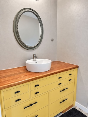 A bathroom with a round mirror, a white sink, and a yellow vanity with drawers. - Big Shell Lake Cabin | Sleeps 8 | Fireplace, Starlink & Private Yard (Shell Lake)