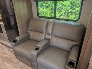 Un sofá modular con portavasos y una ventana con vista a zonas verdes.