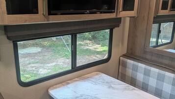 A kitchen area with a marble countertop, a television above cabinets, and a window with a view of greenery.