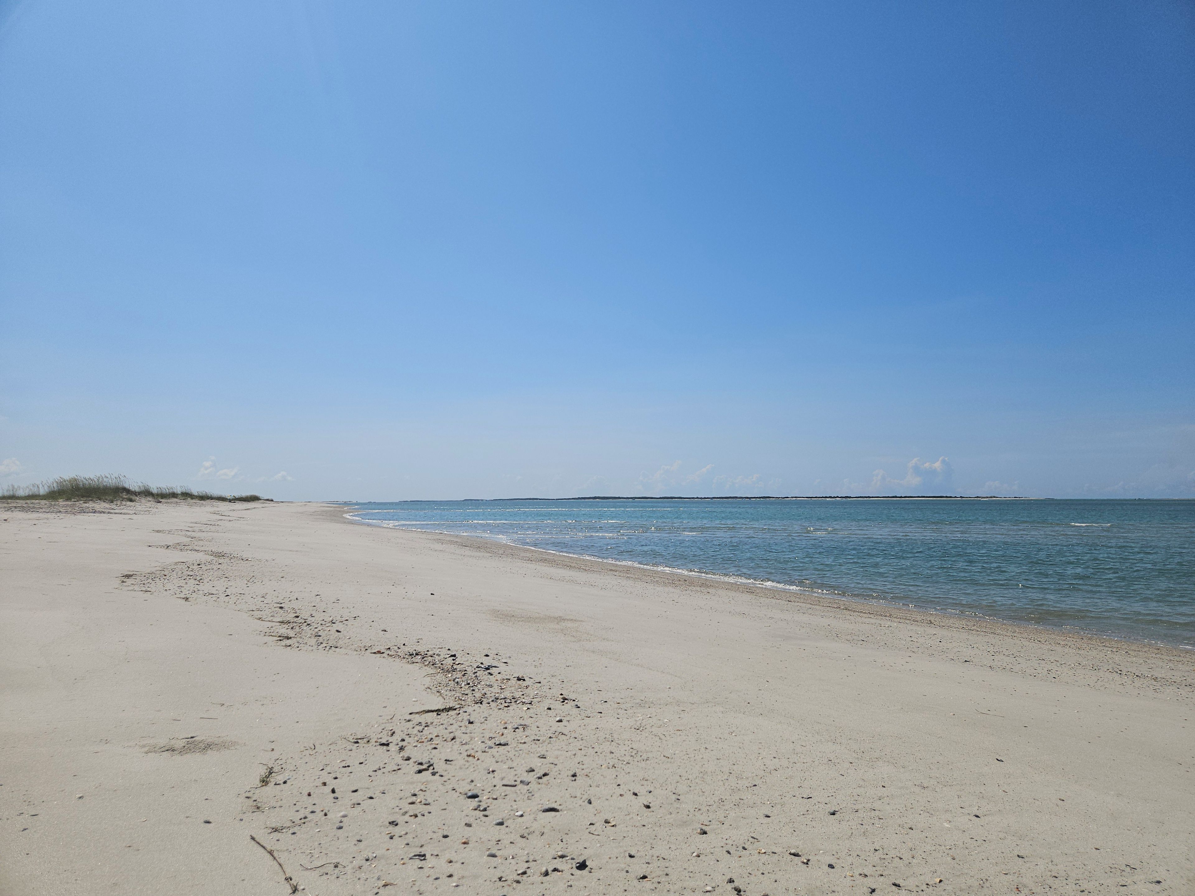 A sandy beach with gentle waves, a clear sky, and distant land.