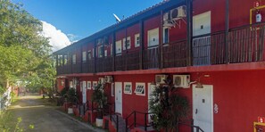 Ein rotes Gebäude mit mehreren Fenstern und Türen, einem Balkon und Klimaanlagen.