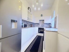 A modern kitchen with white cabinets, a water dispenser, a built-in oven, and a marble backsplash. - Stylish 2-Bed, Weybridge, Sleeps 4, Free Parking (Woburn Hill)
