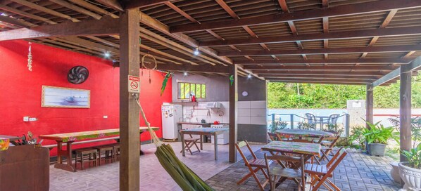 Un espace extérieur abrité, doté de tables et de chaises, avec un mur rouge et un coin cuisine.