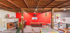 A kitchen with a red wall, a wooden ceiling, and a dining area with a table and chairs. - Suite Tripla com Piscina em Praia de Itamambuca (Ubatuba)