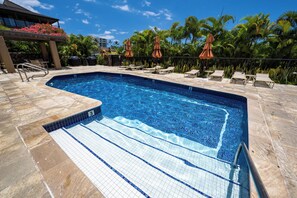 A swimming pool with tiled steps leading into it, surrounded by lounge chairs and umbrellas. - Elua 103 - Lanai View of the ocean- 1 bedroom 2 bath (Kihei)