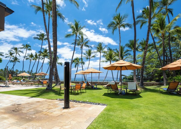 A resort with outdoor seating areas, palm trees, and a view of the ocean. - Elua 103 - Lanai View of the ocean- 1 bedroom 2 bath (Kihei)