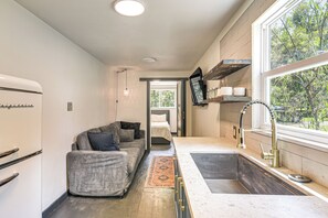 Een compacte keuken met een inbouwoven, een zithoek met een bank, en een groot raam dat voor natuurlijk licht zorgt.
