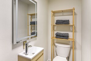Een badkamer met een wit wastafelmeubel, een spiegel, een toilet en een houten handdoekrek met opgevouwen handdoeken.