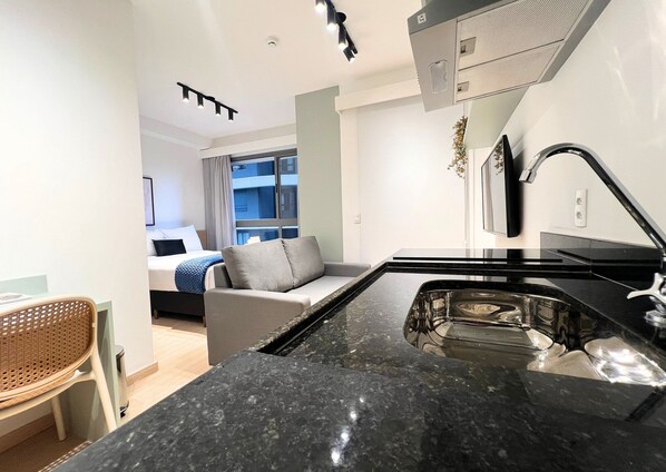A modern kitchen with a black granite countertop, a built-in stove, and a window overlooking a cityscape. - Nex One Edge Pinheiros by Housi (São Paulo)