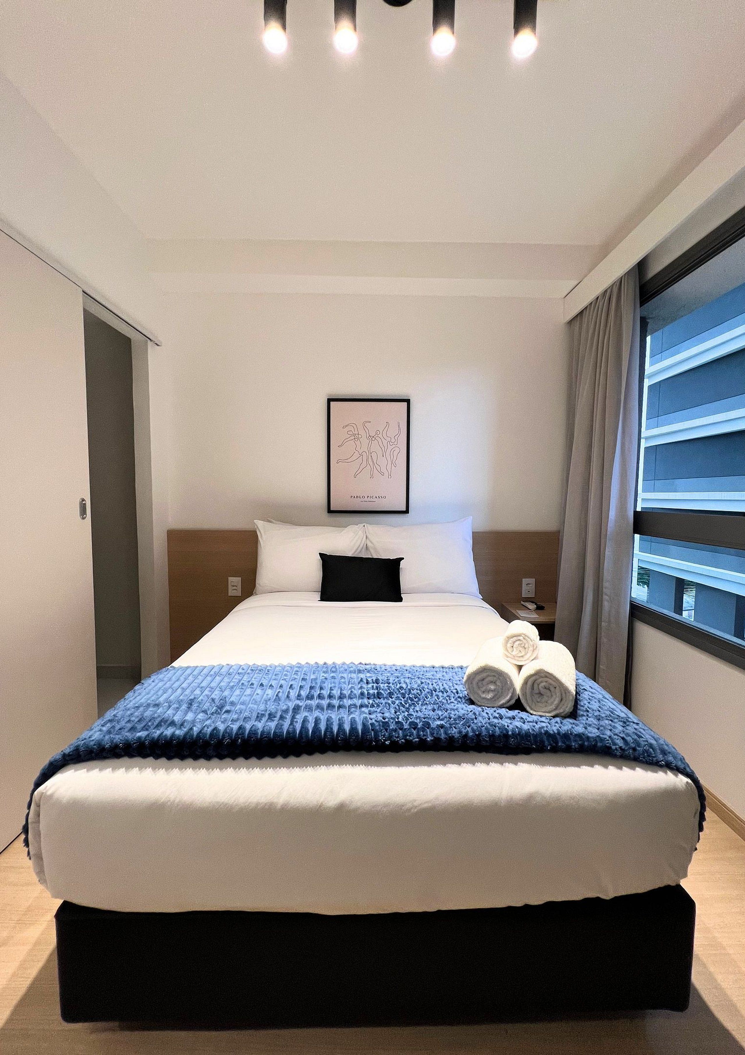 A hotel room with a large bed, a framed artwork on the wall, and a window with curtains.