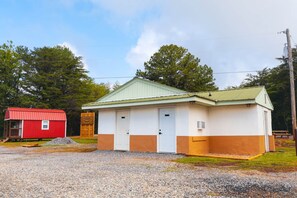 A small, single-story building with a green roof and white and orange walls, located in a rural setting with trees in the background. - Regular RV site (Copperhill)