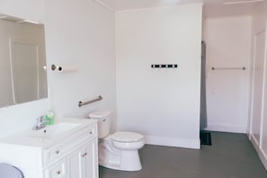 Une salle de bain avec des toilettes blanches, un lavabo avec un miroir et un porte-serviettes.