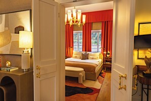 Ein Hotelzimmer mit einem Bett, einem Schreibtisch mit Lampe, einem Sessel und Blick ins Freie durch ein Fenster.