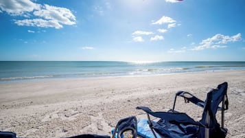 A beach with a clear sky, a calm sea, and a pair of beach chairs.