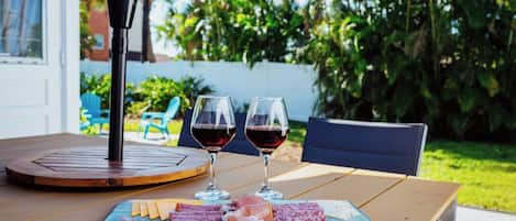 A table with a charcuterie board, two glasses of red wine, and a patio chair.