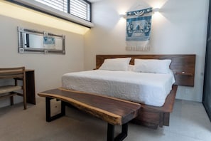 A bedroom with a bed, a bench, a mirror, and a wall hanging. - Villa w/ 800sqft terrace & pool (Puerto Escondido)