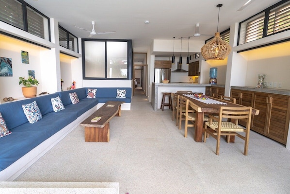 A modern living room with a blue sofa, wooden coffee table, and a dining area with wooden chairs and a table. - Villa w/ 800sqft terrace & pool (Puerto Escondido)