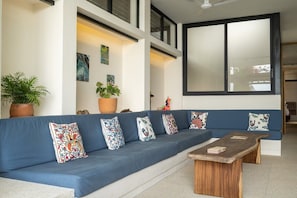 A modern living room with a blue sofa, decorative pillows, a wooden coffee table, and a large window. - Villa w/ 800sqft terrace & pool (Puerto Escondido)