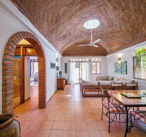 A spacious room with a high ceiling, a dining area with a table and chairs, and a brick archway leading to another room. - Oaxacan home w/ palapa & pool (Puerto Escondido)