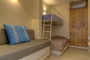 Ein kleines Zimmer mit einem Etagenbett, einer Couch mit Kissen, einem Holzschrank und einer wandmontierten Klimaanlage.