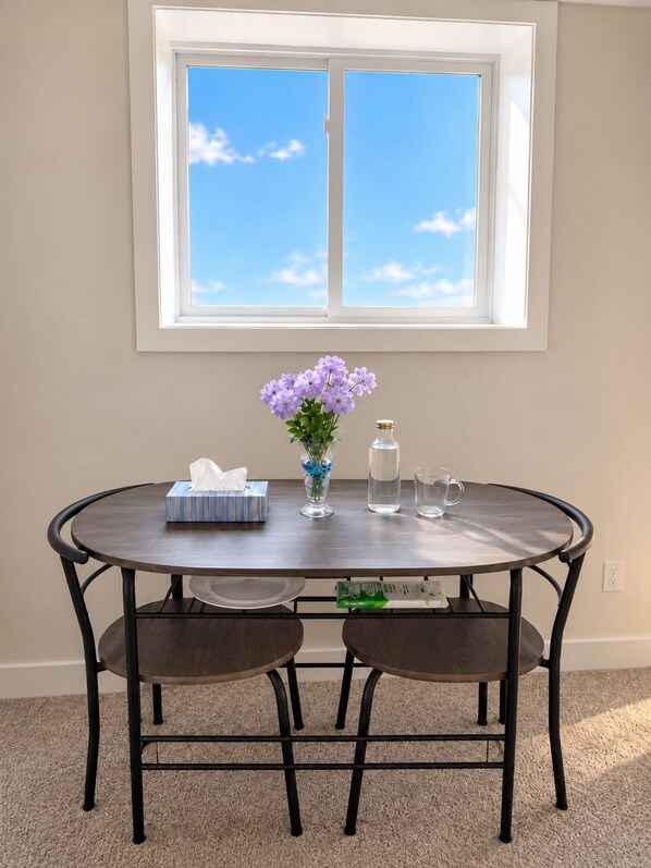 A round dining table with two chairs, a vase with purple flowers, a tissue box, a bottle, and two glasses.