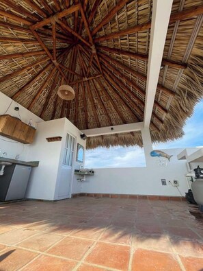 A covered outdoor area with a thatched roof, a sink, and a window. - Rooftop pool, sunsets & sea view (Puerto Escondido)