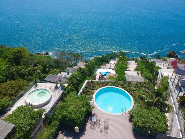 A resort with two swimming pools surrounded by lush greenery and a view of the ocean.