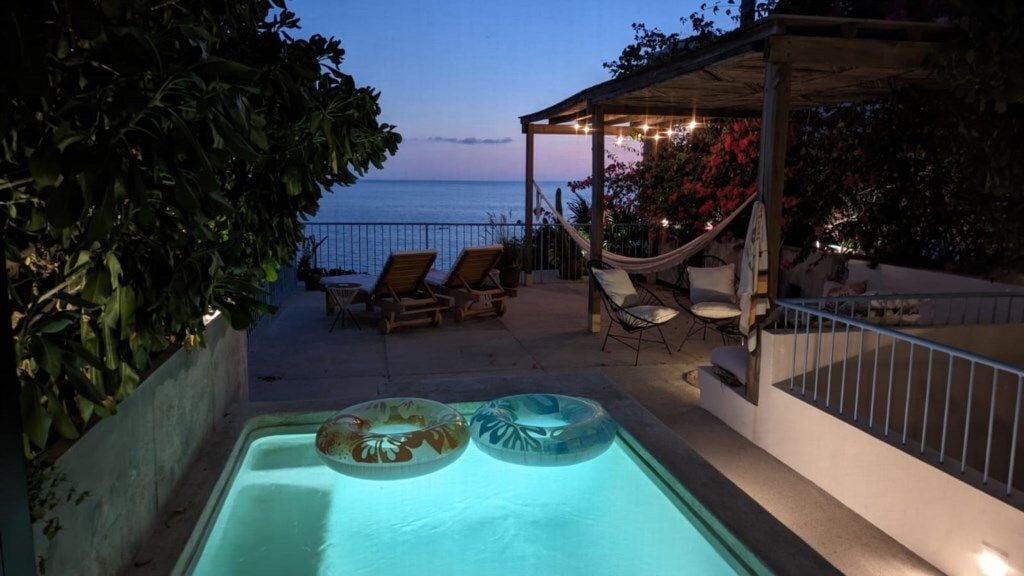 Una piscina exterior con sillones de descanso y vistas al mar al atardecer.