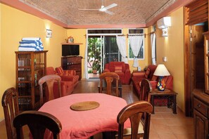 A living room with a dining area, a television, and a ceiling fan. - Oaxacan home w/ palapa, sea view (Puerto Escondido)