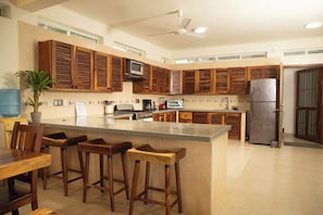 A modern kitchen with wooden cabinets, a central island with stools, a refrigerator, and a ceiling fan. - Sea-view condo w/ 2 king suites (Puerto Escondido)
