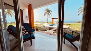 Ein Zimmer mit Glastür, das auf eine Terrasse mit zwei blauen Stühlen und einem kleinen Pool führt.