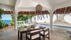 A covered outdoor dining area with a pool, white pillars, and a view of the sea. - 🌊 Ocean-View Apartment with Spacious Terraces (Puerto Escondido)