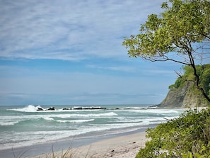 A beach with waves, a cliff, and greenery. - Ocean View Studio Home, Samara Nosara Sal Vida 2 (Naranjal)