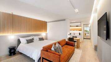 A modern hotel room with a bed, sofa, and a view of the kitchen and balcony.