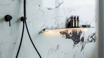 A modern bathroom with a marble wall, a handheld showerhead, and a shelf with toiletries.