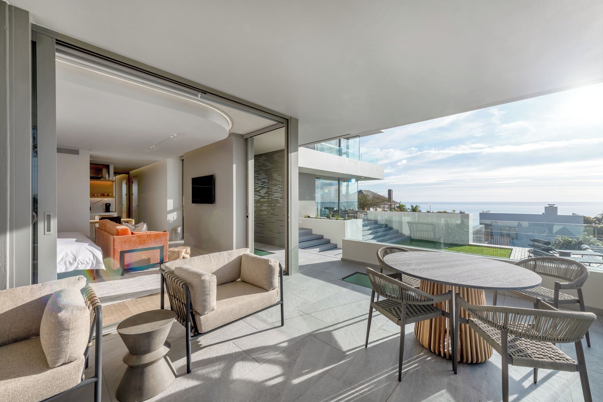 A modern hotel room with a balcony, furnished with a sofa, chairs, and a table.
