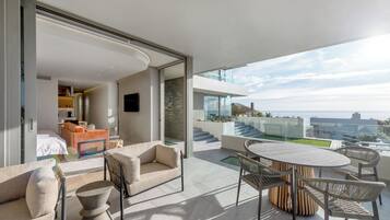 A modern hotel room with a balcony, furnished with a sofa, chairs, and a table.